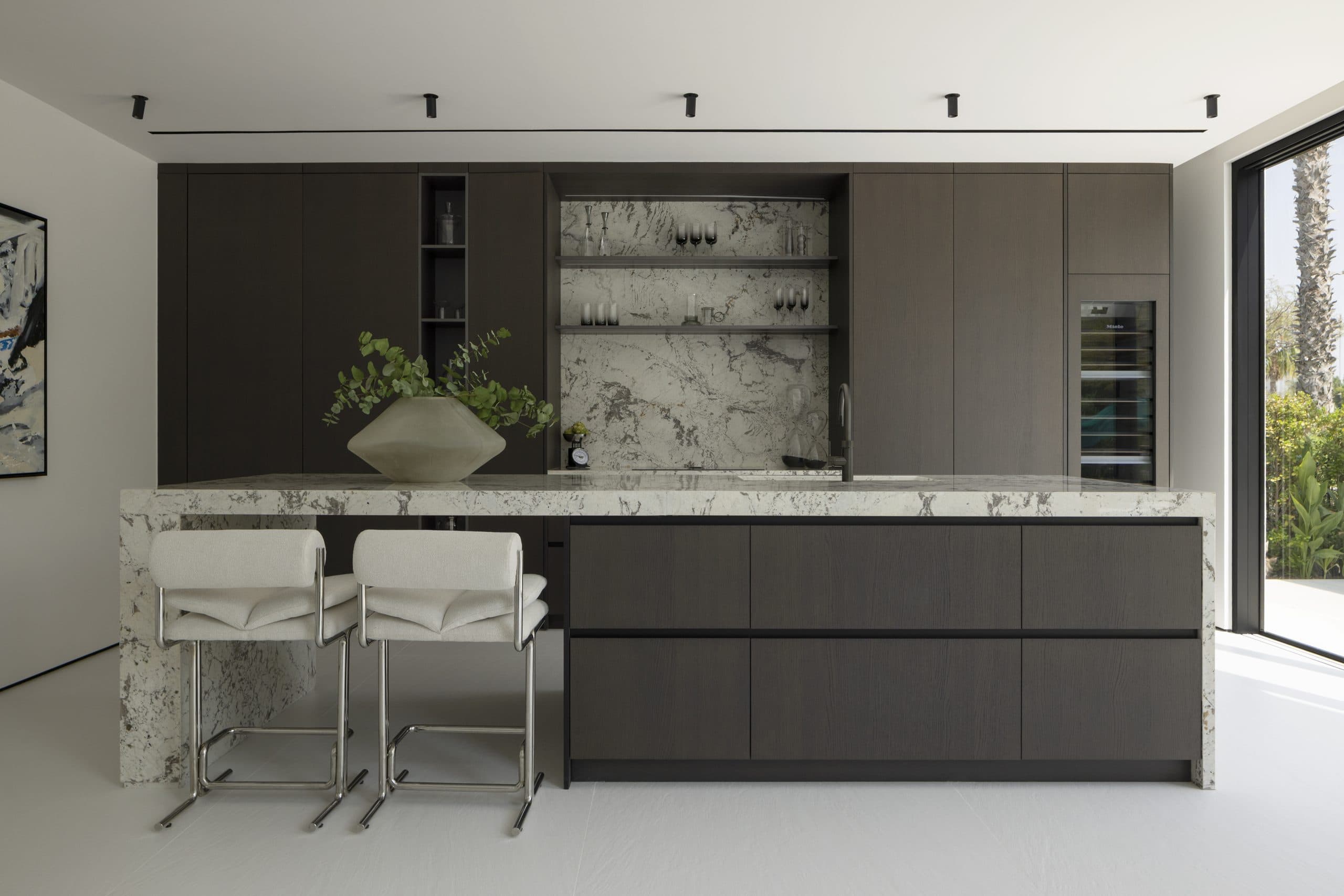 Kitchen with dark oak tall units and a marble-clad island at Villa 16, Jumeirah Islands